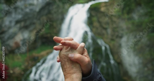 Elderly couple hiking in mountains and high fiving after reaching the top with waterfall. Retirement, active lifestyle and sport. photo