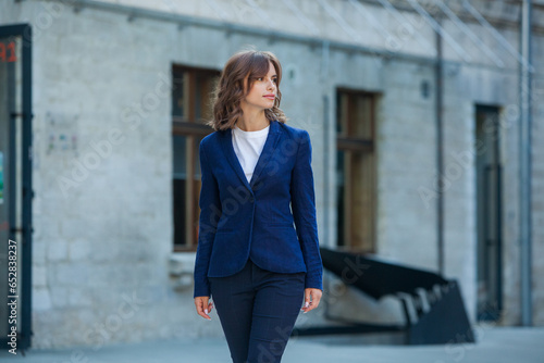 Portrait of a successful business woman in front of modern business building. Young manager poses outside. Woman employee of an office.
