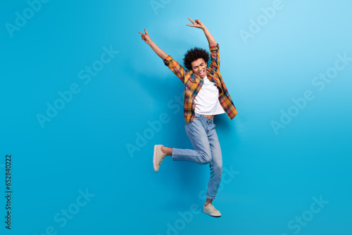Full length photo of excited cool guy dressed checkered shirt dancing showing v-signs empty space isolated blue color background