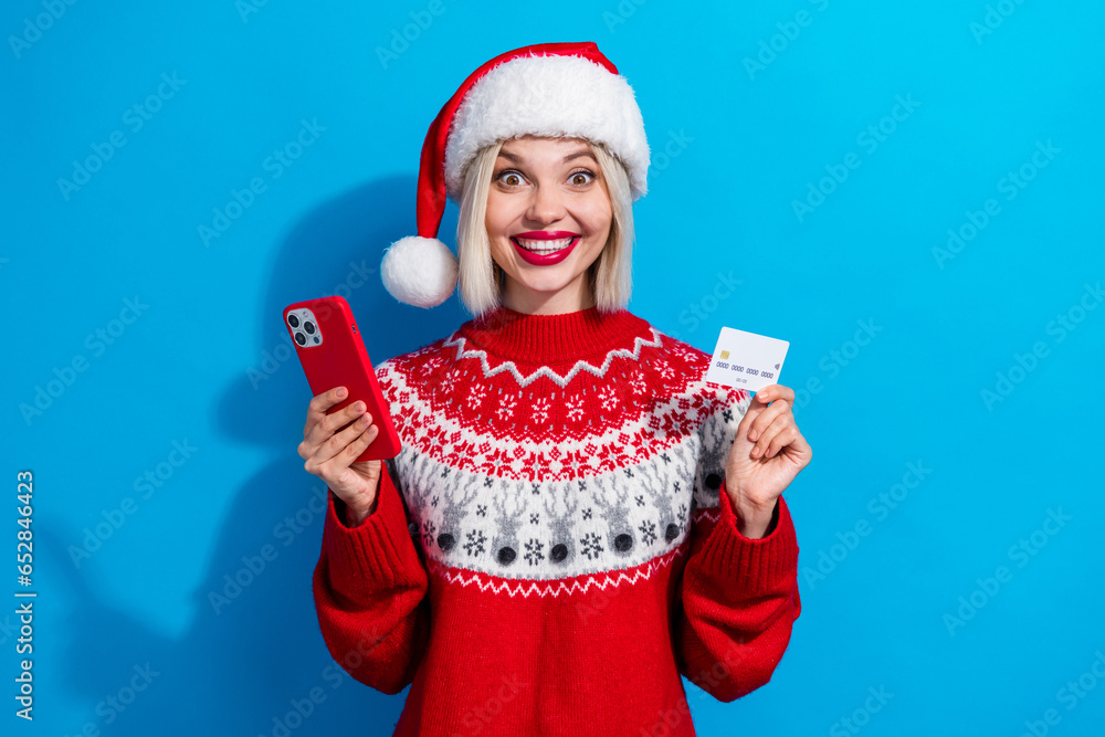 Obraz premium Photo of attractive positive person hold smart phone wireless debit card wear red x-mas eve jumper isolated on blue color background