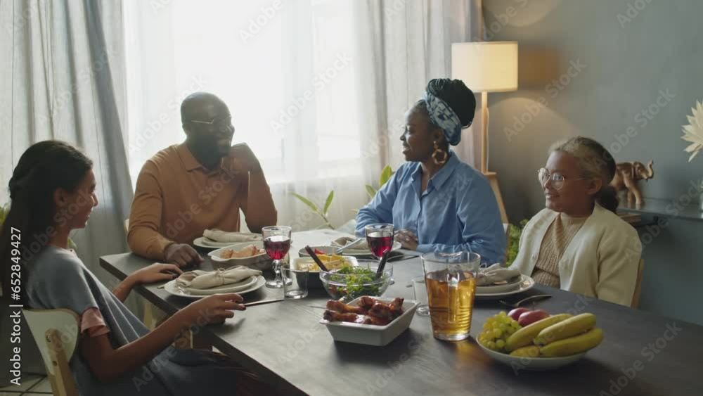 African American mother, father and two daughters sitting around dinner table, holding hands and praying with eyes closed before eating meal on Kwanzaa holiday African American mother, father and two daughters sitting around dinner table, holding hands and praying with eyes closed before eating meal on Kwanzaa holiday