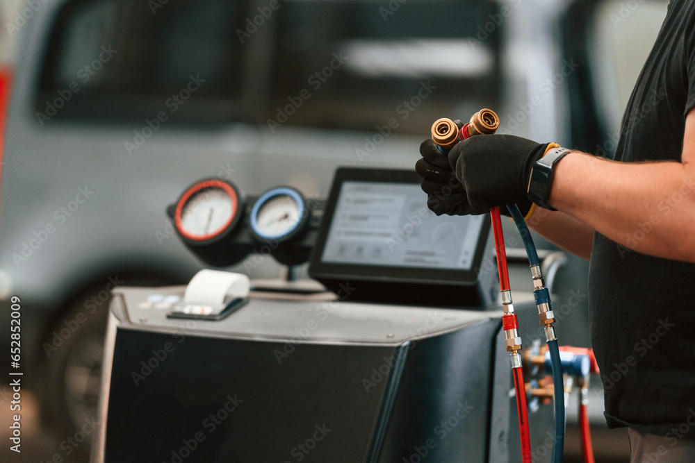 With wires in hands. Man is works in the automobile repairing salon