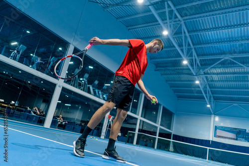 young man on an indoor tennis court hitting the ball with a racket serving during a game tennis instructor professional sport