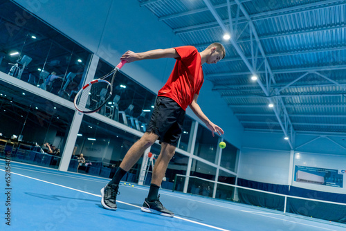 young man on an indoor tennis court hitting the ball with a racket serving during a game tennis instructor professional sport