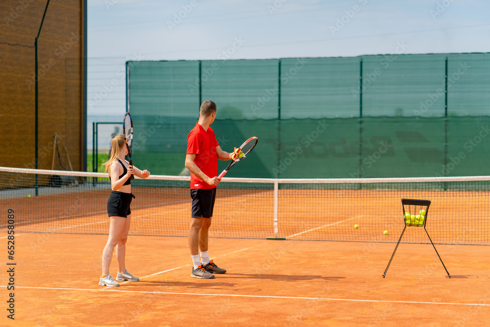 a young coach teaches a beginner girl to play tennis, practice movements with a racket practice with a ball on a tennis court