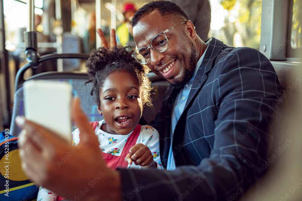 Young African American businessman using a smartphone with his daughter while taking her to school on the bus Young African American businessman using a smartphone with his daughter while taking her to school on the bus