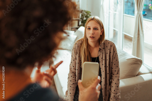 Young woman confronting her lesbian partner after discovering affectionate text messages to a another person on her smartphone in the living room at home photo