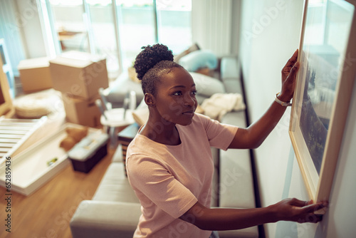 Young African American woman positioning a painting on the wall after moving in her new apartment