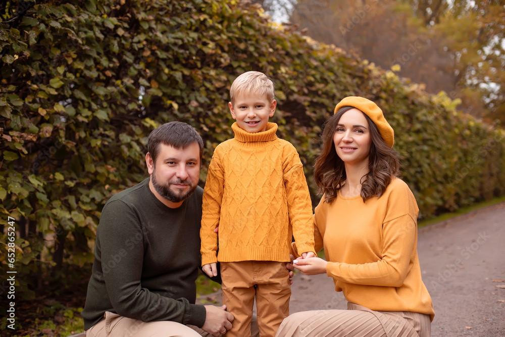Fototapeta premium Portrait of a beautifully dressed family, mom in an orange beret, dad and 7 year old son in an autumn park.
