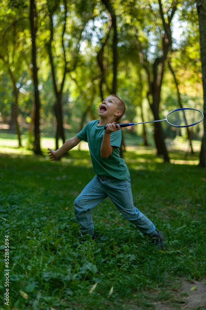 little cute boy playing badminton in a summer park, surrounded by green trees little cute boy playing badminton in a summer park, surrounded by green trees