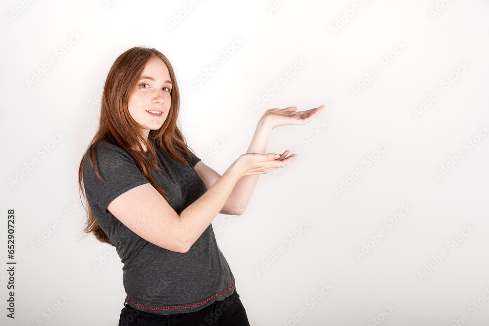 Young red haired woman wearing a grey shirt over isolated white background smiling at the camera while presenting with her hands Young red haired woman wearing a grey shirt over isolated white background smiling at the camera while presenting with her hands