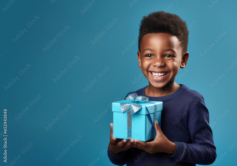 Handsome African American happy little boy holding holiday gift box with bow and ribbon, surprise happy birthday greeting, mother's father's day on blue background Handsome African American happy little boy holding holiday gift box with bow and ribbon, surprise happy birthday greeting, mother's father's day on blue background