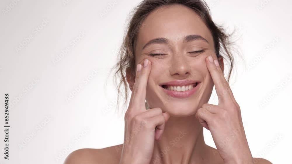 Young brunette woman massaging and touching her face after applying cream. Natural healthy face. Close up. Concept for fresh moisturized elasticity skin. Healthy model on white background in studio. Young brunette woman massaging and touching her face after applying cream. Natural healthy face. Close up. Concept for fresh moisturized elasticity skin. Healthy model on white background in studio.
