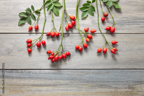 Rosehip branches with red berries on wooden table.