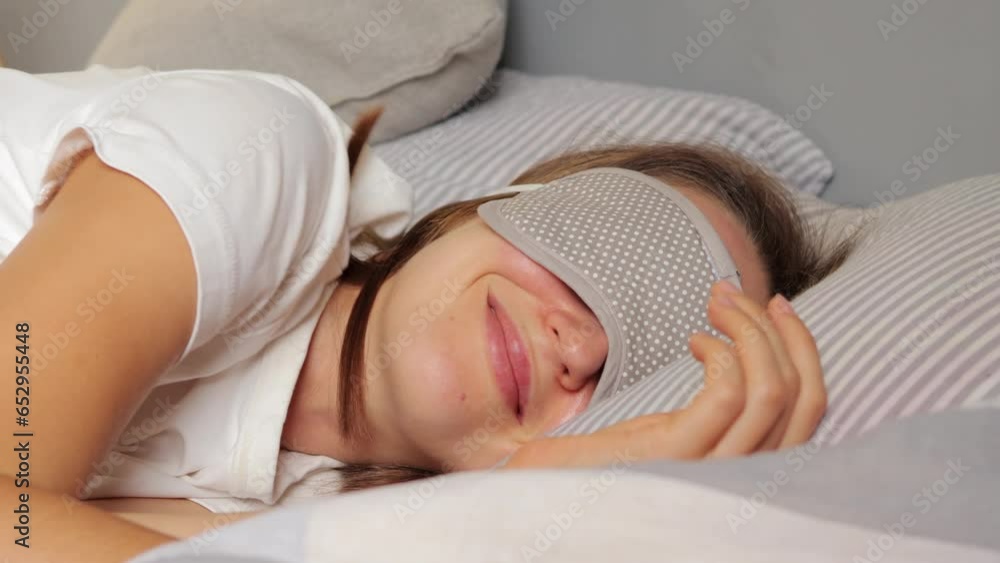 Beautiful young woman sleeping in her bed at home smiling sees positive dreams wearing white t-shirt and blindfold weekend laziness morning relaxion.