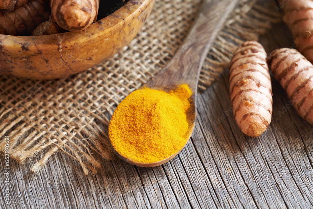Curcuma powder with fresh turmeric root on a table Curcuma powder with fresh turmeric root on a table