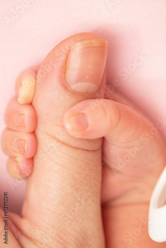 Baby and mother creative minimal concept. The baby is holding the mother's finger on a pastel pink background. Close up, macro shot 