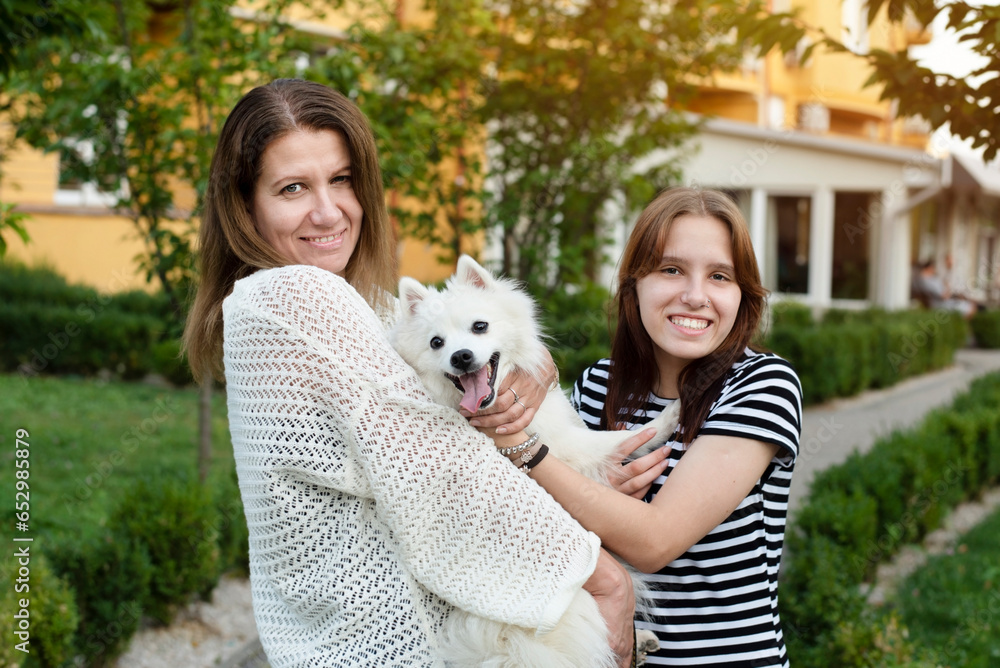 The dog feels good in arms of its owners, mother and teenage daughter are talking, having fun and taking pictures with their dog, friendship with a dog brings mother and daughter together The dog feels good in arms of its owners, mother and teenage daughter are talking, having fun and taking pictures with their dog, friendship with a dog brings mother and daughter together