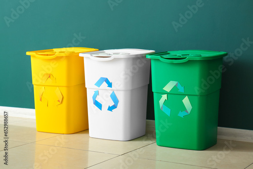 Different garbage bins with recycling symbol near green wall