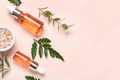 Bottles of cosmetic oil with plant twigs and sea salt on beige background