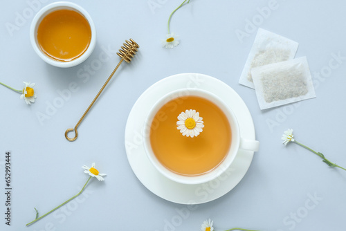 Cup of hot tea with honey and flowers on pale blue background © Pixel-Shot