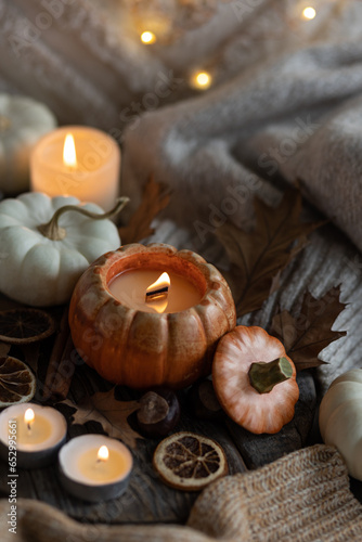 Cozy autumn home still life scene. Ceramic handmade pumpkin mug with burning candle near the window. Fall mood  Thanksgiving concept. Pumpkins  dry leaves  wool sweater  wooden background
