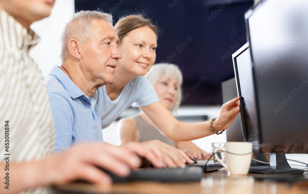 Obraz premium Concerned old man sitting at computer while trainer explaining him something during IT courses