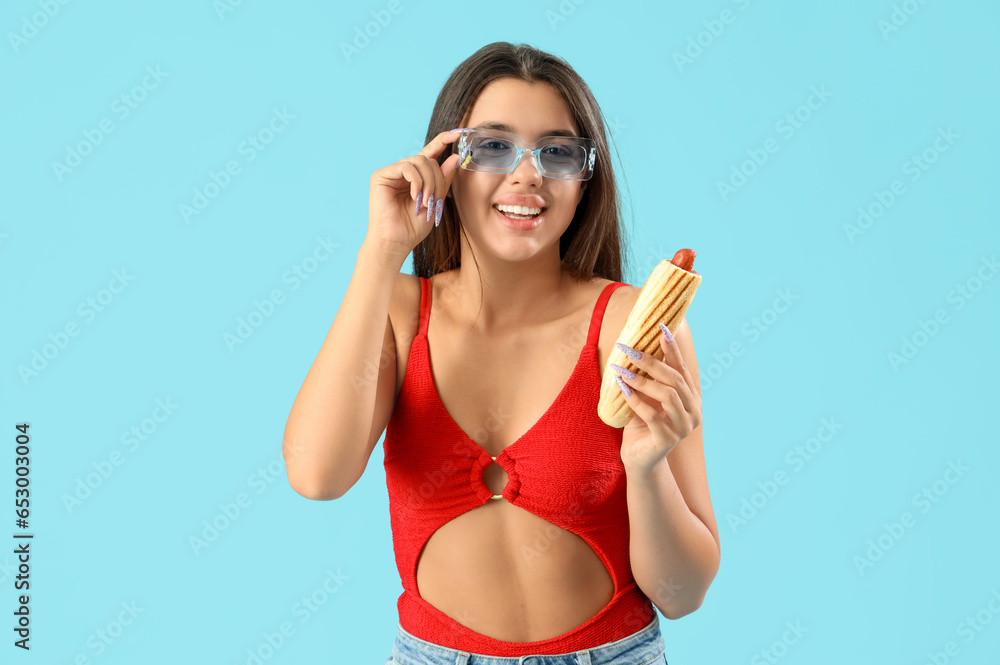 Pretty young woman in beachwear and with tasty french hot dog on blue background Pretty young woman in beachwear and with tasty french hot dog on blue background