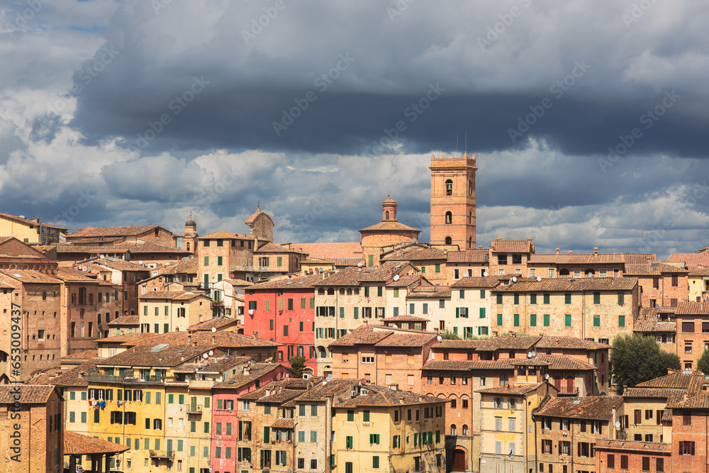 Colourful and scenic townscape view of historic hilltop village of Siena against a moody sky in Tuscany, Italy.