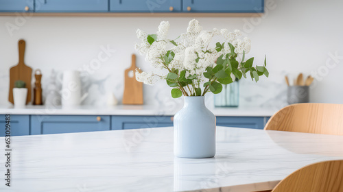 Vase with fresh spring flowers on dinning table on the background of modern kitchen in Scandinavian interior style. Light white blue colors. 
