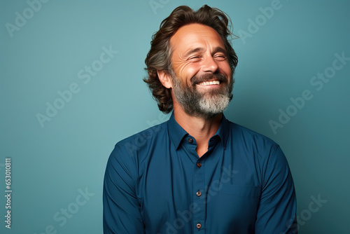 middle age man wearing a blue shirt looking to the side smiling in against a green background