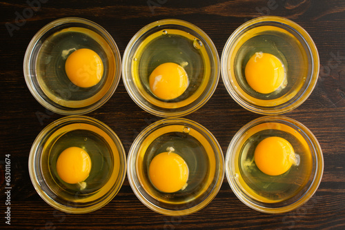 Cracked Eggs in Prep Bowls: Six cracked eggs in small glass bowls on a wooden table photo