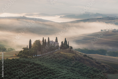 Atmospheric sunrise mist through the valley of Val d Orcia and a rustic farmhouse in the scenic countryside landscape and rolling hills of rural Tuscany  Italy.