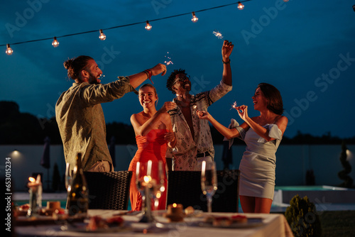 Fotografie Friends dancing and drinking by the poolside at night