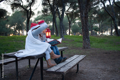 2024CFCFamilia, two siblings with papa noel cap reading with a lattern in a forest. Winter. Christmas.  Horizontal photo