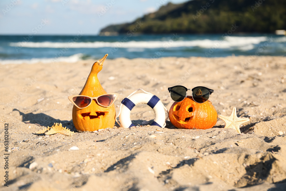 Obraz premium Carved pumpkins for Halloween with lifebuoy, stylish sunglasses and starfishes on beach
