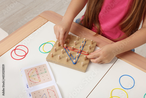 Motor skills development. Girl playing with geoboard and rubber bands at white table, closeup