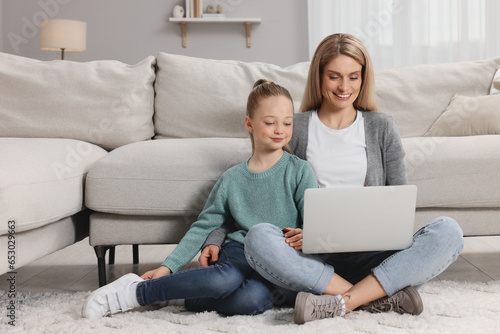 Happy woman and her daughter with laptop on floor at home