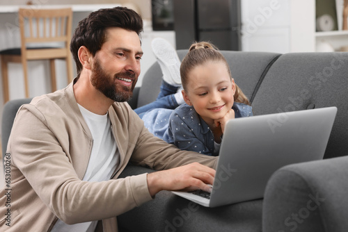 Happy man and his daughter with laptop on sofa at home