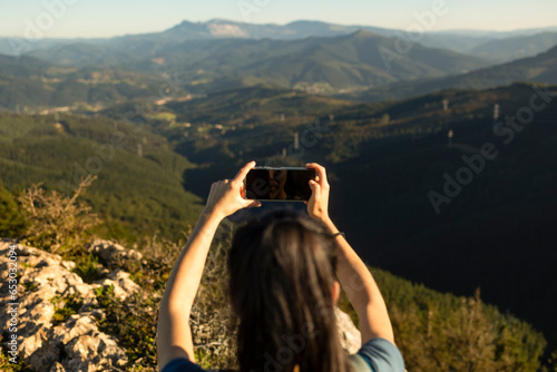 A happy young woman takes pictures of the landscape with her smartphone from the top of a mountain. photo