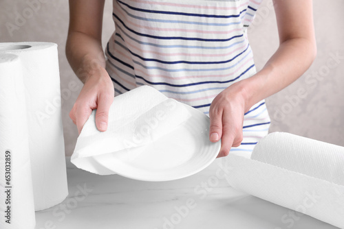 Woman wiping plate with tissue paper at white marble table, closeup