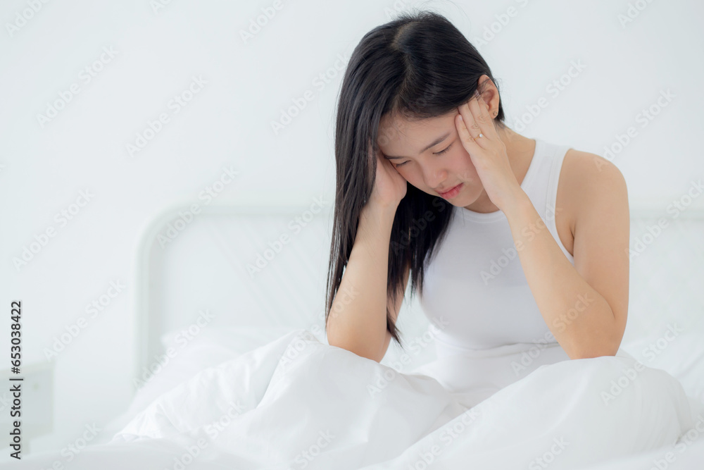 Young asian woman sitting on bed pain headache in the bedroom at home, unhappy female exhaustion and sick headache, anxiety and unwell, dizziness and disorder, medical and health concept. Young asian woman sitting on bed pain headache in the bedroom at home, unhappy female exhaustion and sick headache, anxiety and unwell, dizziness and disorder, medical and health concept.