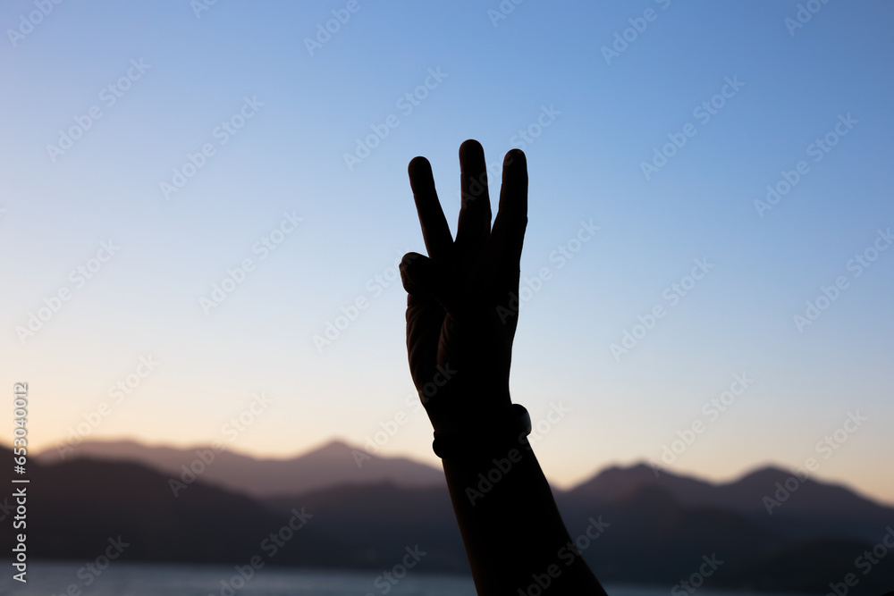 silhouette of hands in the shape of the number three with a beautiful colorful late afternoon sky in Rio de Janeiro.