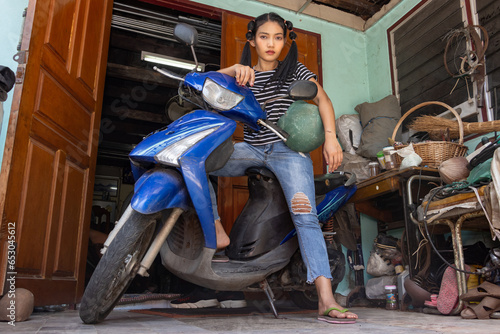 A young woman is standing by a motorcycle parked in front of the entrance to a house