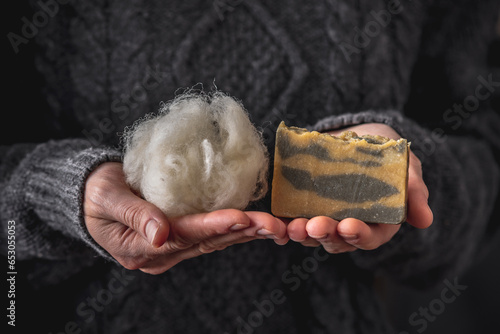 Woman in a warm gray sweater holds a little white wool in one hand and a piece of natural cashmere soap in the other hand