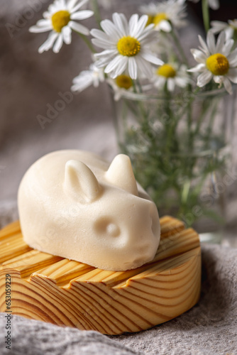 Natural handmade soap in the shape of cute rabbits on a wooden soap dish on a background of chamomile flowers. Concept of using eco friendly products for the care of delicate baby skin