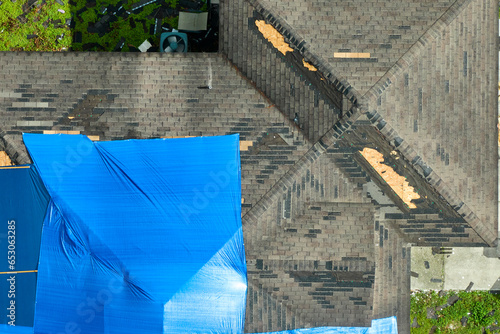 Aerial view of damaged in hurricane Ian house roof covered with blue protective tarp against rain water leaking until replacement of asphalt shingles