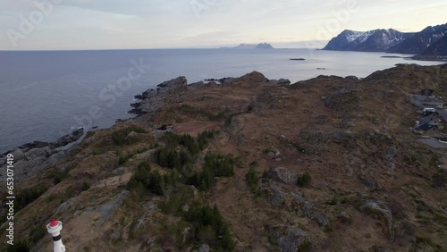 Aerial backwards shot of a old lighthouse in Northern Norway Lofoten with snowy mountains in the background  and view to Varoy photo