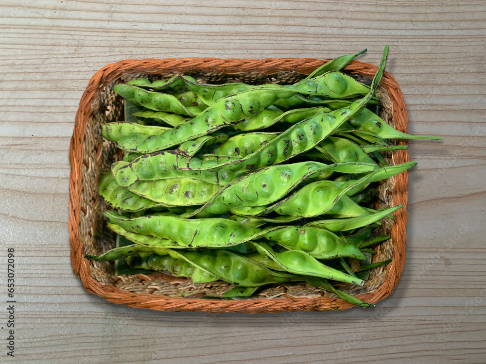 Raw parkia speciosa or petai, pete bitter bean, twisted cluster bean, stinker or stink bean, in a woven wooden basket Raw parkia speciosa or petai, pete bitter bean, twisted cluster bean, stinker or stink bean, in a woven wooden basket