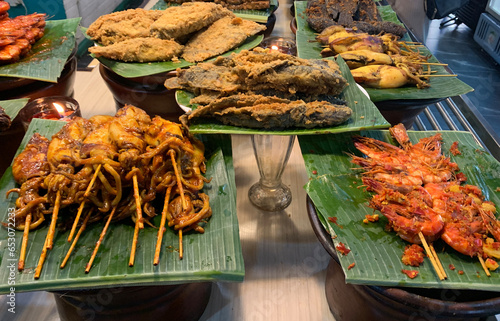 Set of Sundanese side dishes or hidangan sunda, consisting of grilled fish, grilled squid, and satay, served on banana leaf. photo
